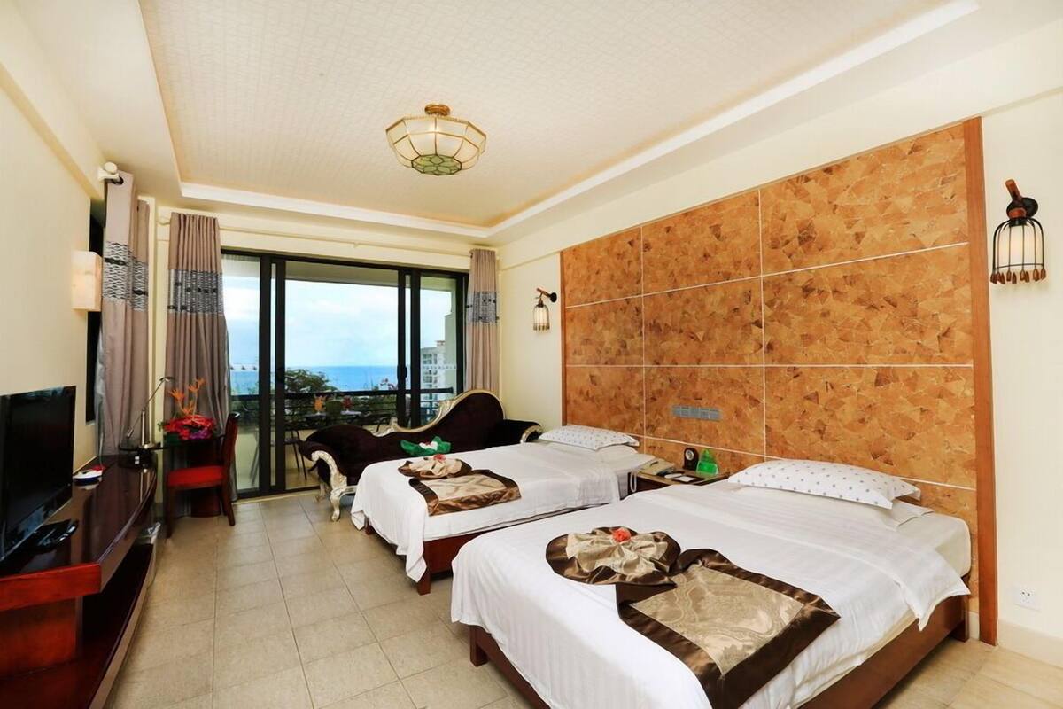 Quarto de hotel com duas camas, televisão, área de refeições e vista para o mar.