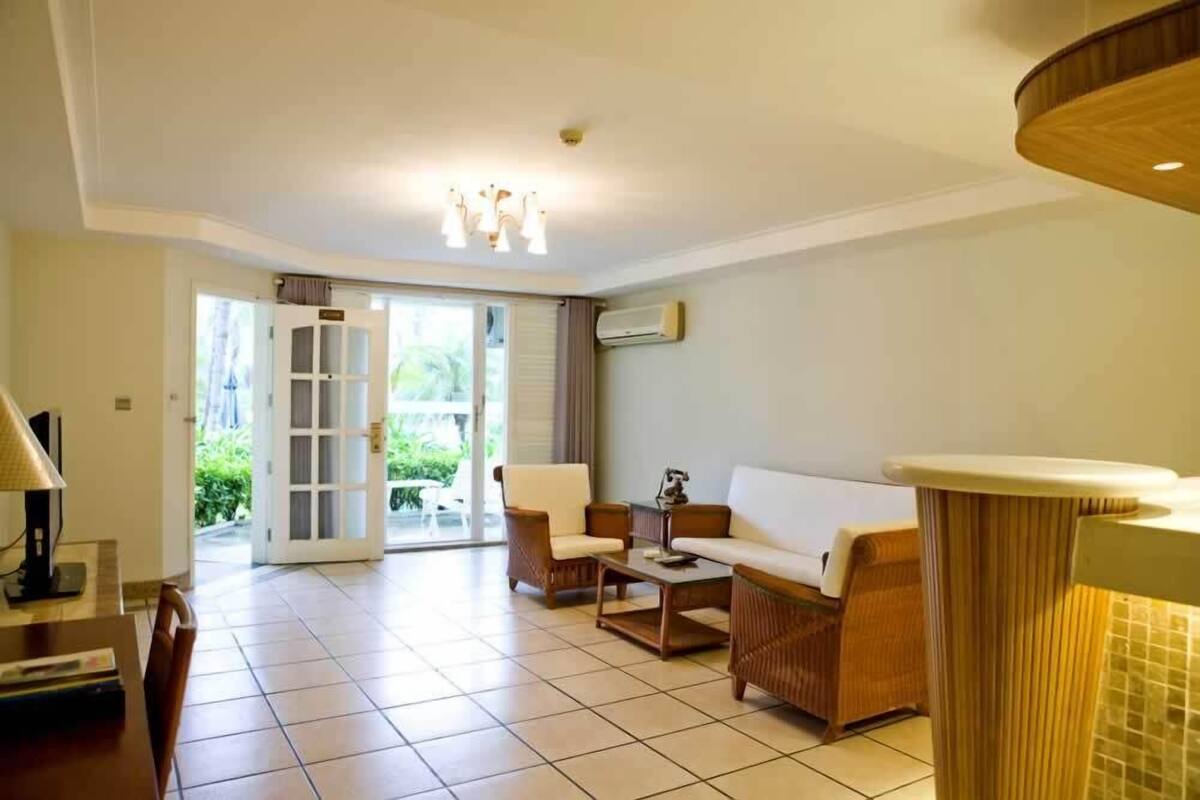 Ampla sala de estar com sofá, cadeiras e mesa de centro. Há uma porta que dá para área externa com vista para áreas verdes.