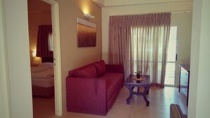 A living room with a sofa, a small table with a plant, and a painting on the wall. - Kibbutz Tiratzvi - Country Lodging (Emek HaMaayanot)