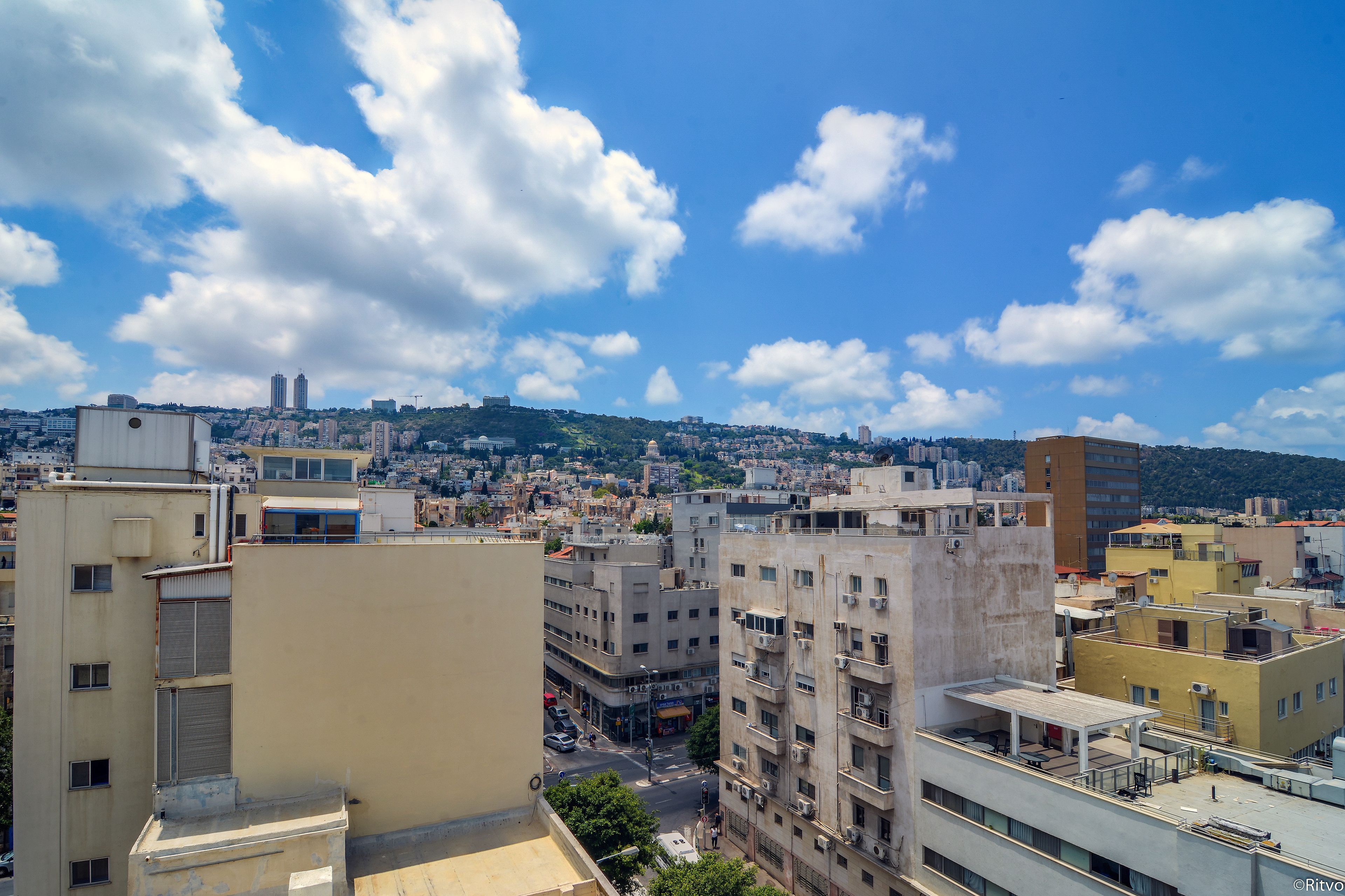 A cityscape with multiple buildings, a clear sky, and a distant hill.