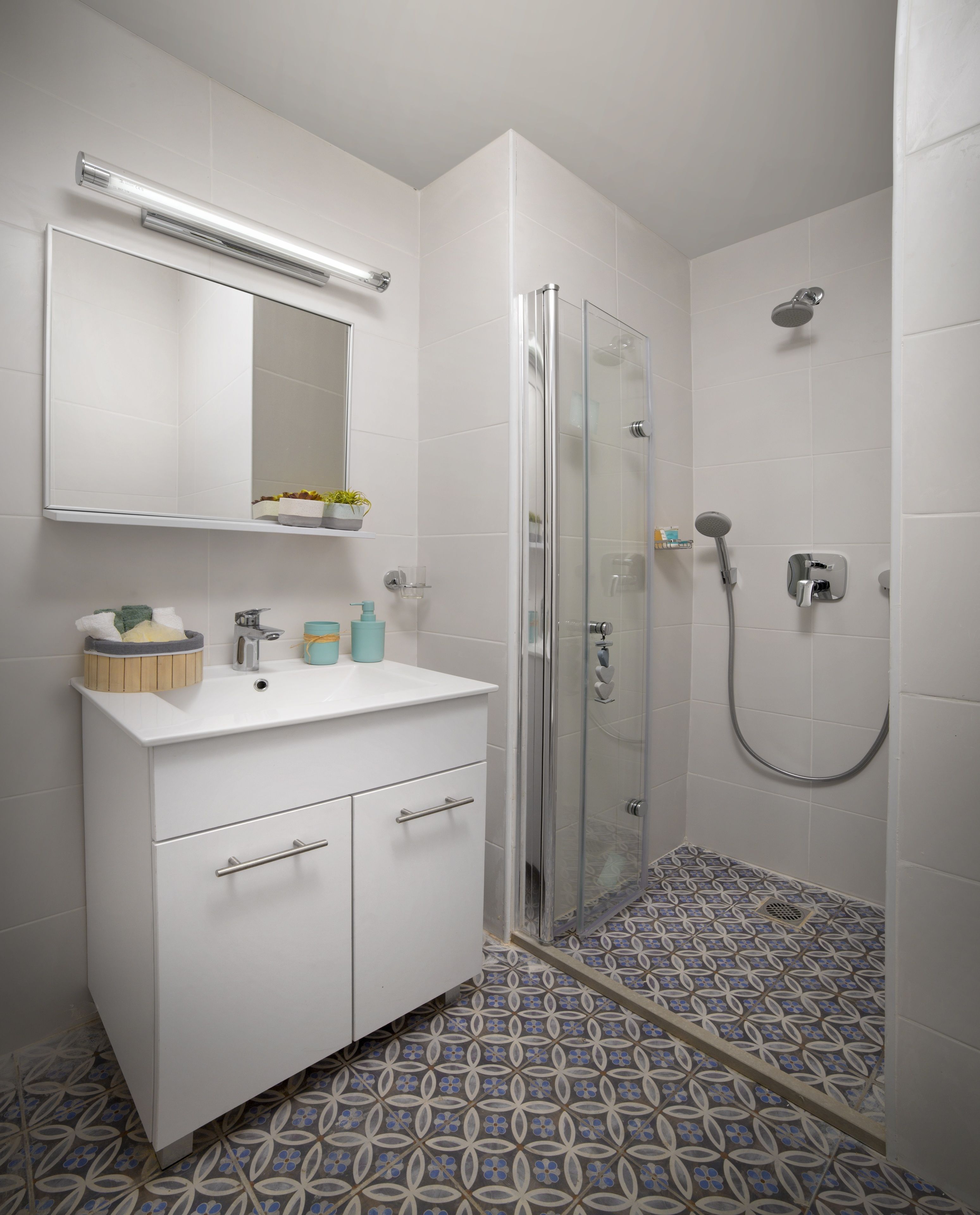 A bathroom with a white vanity, a glass shower enclosure, and patterned floor tiles.