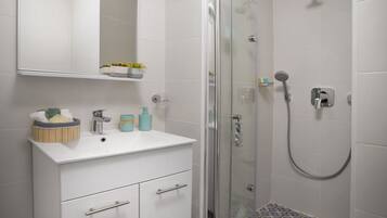 A bathroom with a white vanity, a glass shower enclosure, and patterned floor tiles.
