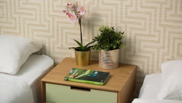 A neatly made bed with white linens, a small wooden nightstand with a green drawer, and two potted plants.