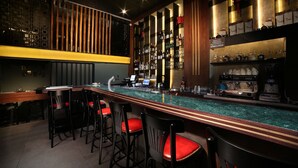 A bar area with a long counter, multiple stools, and shelves stocked with bottles and glasses. - Diana Hotel (Haifa)