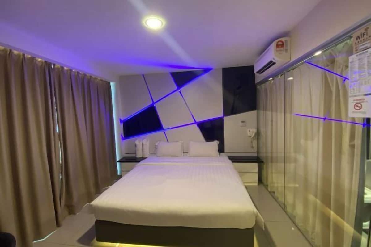A modern hotel room with a bed, a bedside table, a window with curtains, and a wall-mounted air conditioning unit.