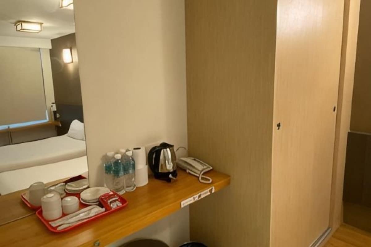 Una habitación de hotel con un escritorio de madera, un espejo, una cama y una puerta.
