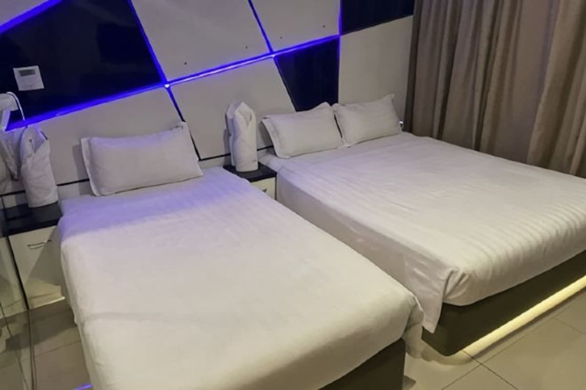 Una habitación de hotel con dos camas, un cabecero moderno y una mesita de noche con una lámpara.