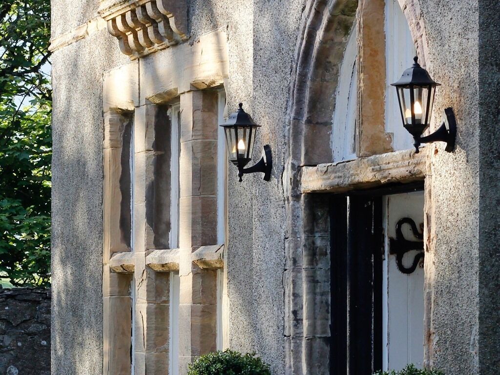 A stone building with large windows and two wall-mounted lanterns.