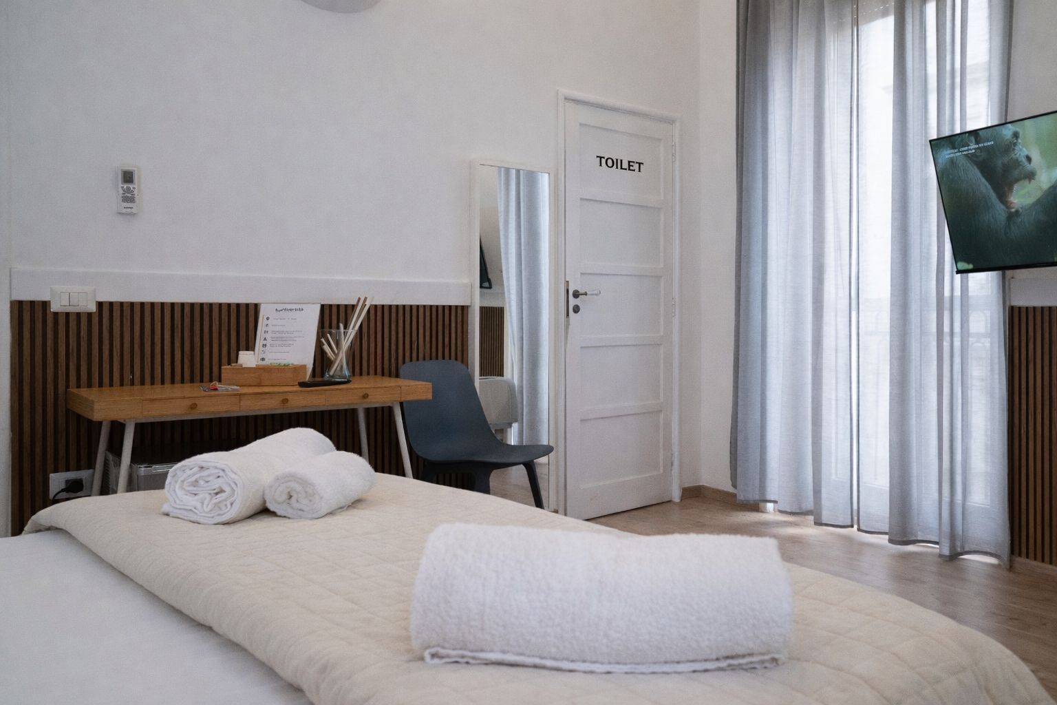 A hotel room with a bed, a desk with a chair, a TV, and a toilet.
