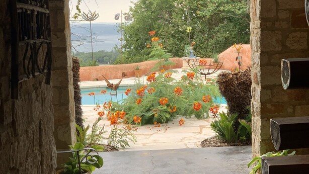 An arched doorway leading to a pool area with a view of the sea, surrounded by lush greenery and potted plants. - Hudson Bend Casa at Lake Travis Owned by famous chef (Austin)