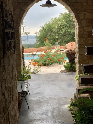 An arched doorway leading to a pool area with a view of the sea, surrounded by lush greenery and potted plants.