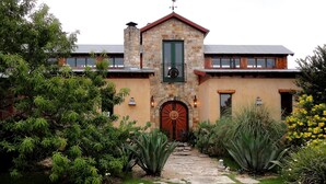 A stone building with a central entrance, a small balcony, and a garden with various plants. - Hudson Bend Casa at Lake Travis Owned by famous chef (Austin)