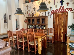A dining area with a wooden table and chairs, a cabinet with dishes, and a wall decorated with crosses and religious icons.