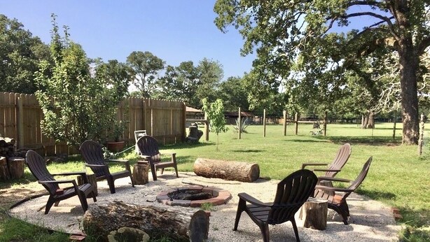 An outdoor seating area with Adirondack chairs, a fire pit, and a wooden table.