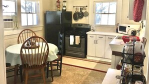 A compact kitchen with a refrigerator, stove, microwave, and a dining table with chairs.