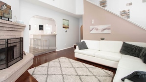 Una sala de estar moderna con chimenea, sofá blanco y una escalera que lleva a un nivel superior.