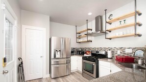 Una cocina moderna con electrodomésticos de acero inoxidable, repisas de madera y encimera de granito.