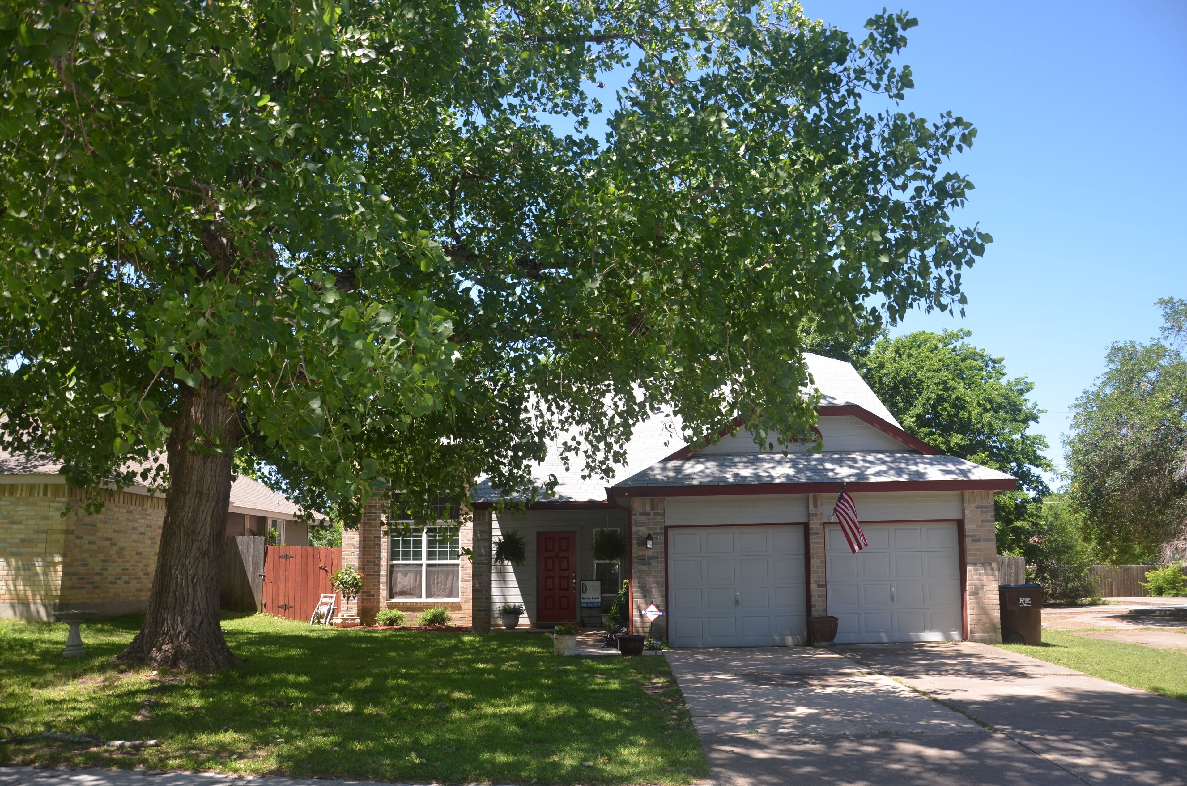 A two-story house with a garage, a front yard, and a large tree providing shade.