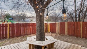 Una terraza de madera con un banco, un árbol y luces colgantes.