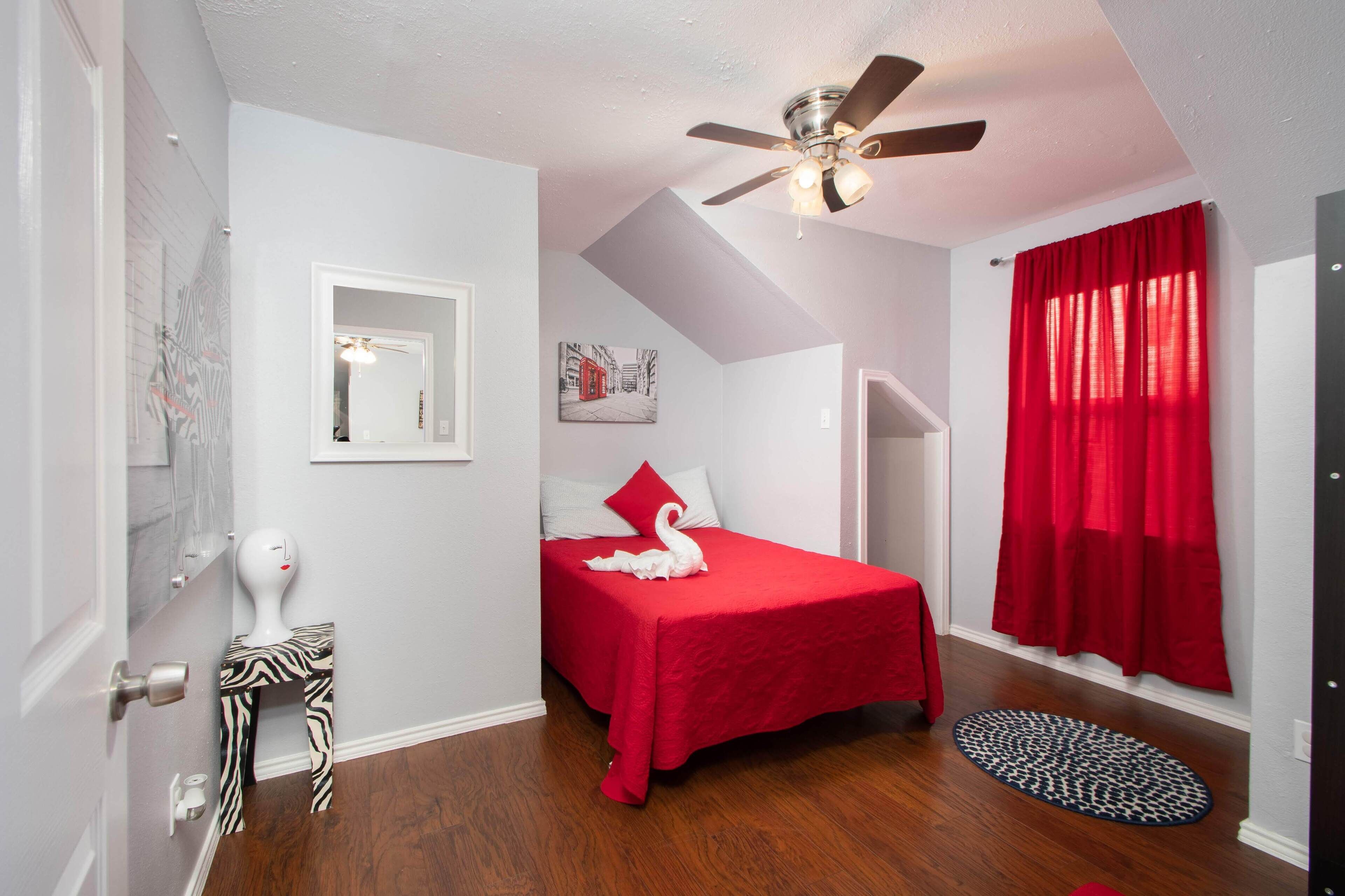 A bedroom with a bed, a ceiling fan, a red curtain, a zebra-patterned stool, and a round rug.
