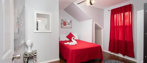 A bedroom with a bed, a ceiling fan, a red curtain, a zebra-patterned stool, and a round rug.