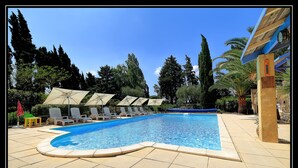 Piscina com espreguiçadeiras e guarda-sóis, cercada por árvores e um céu limpo.