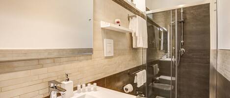 Een moderne badkamer met een groot wastafelmeubel, een douchecabine met glazen wanden en een toilet.