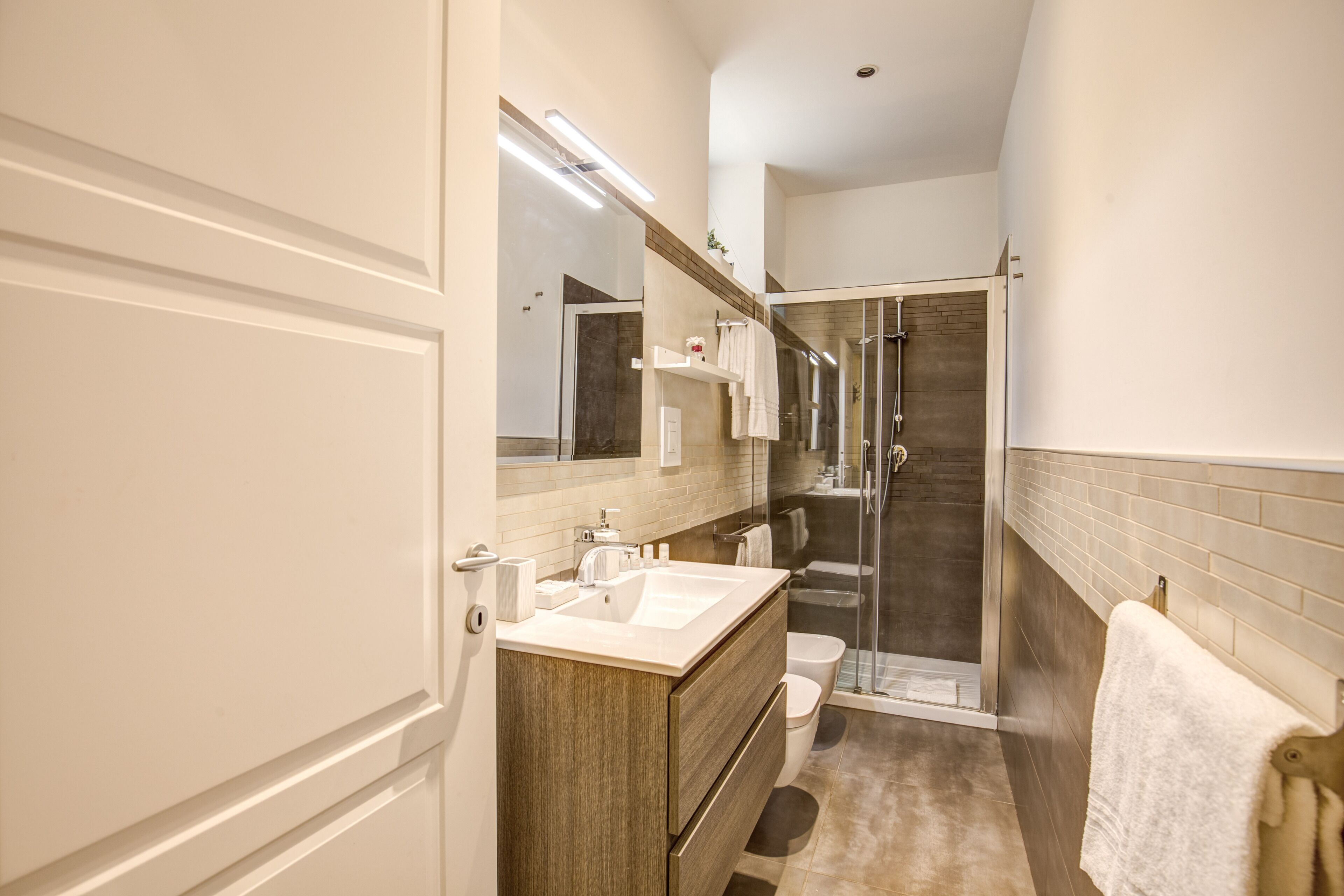 A modern bathroom with a large mirror, wooden vanity, white sink, and a glass-enclosed shower.