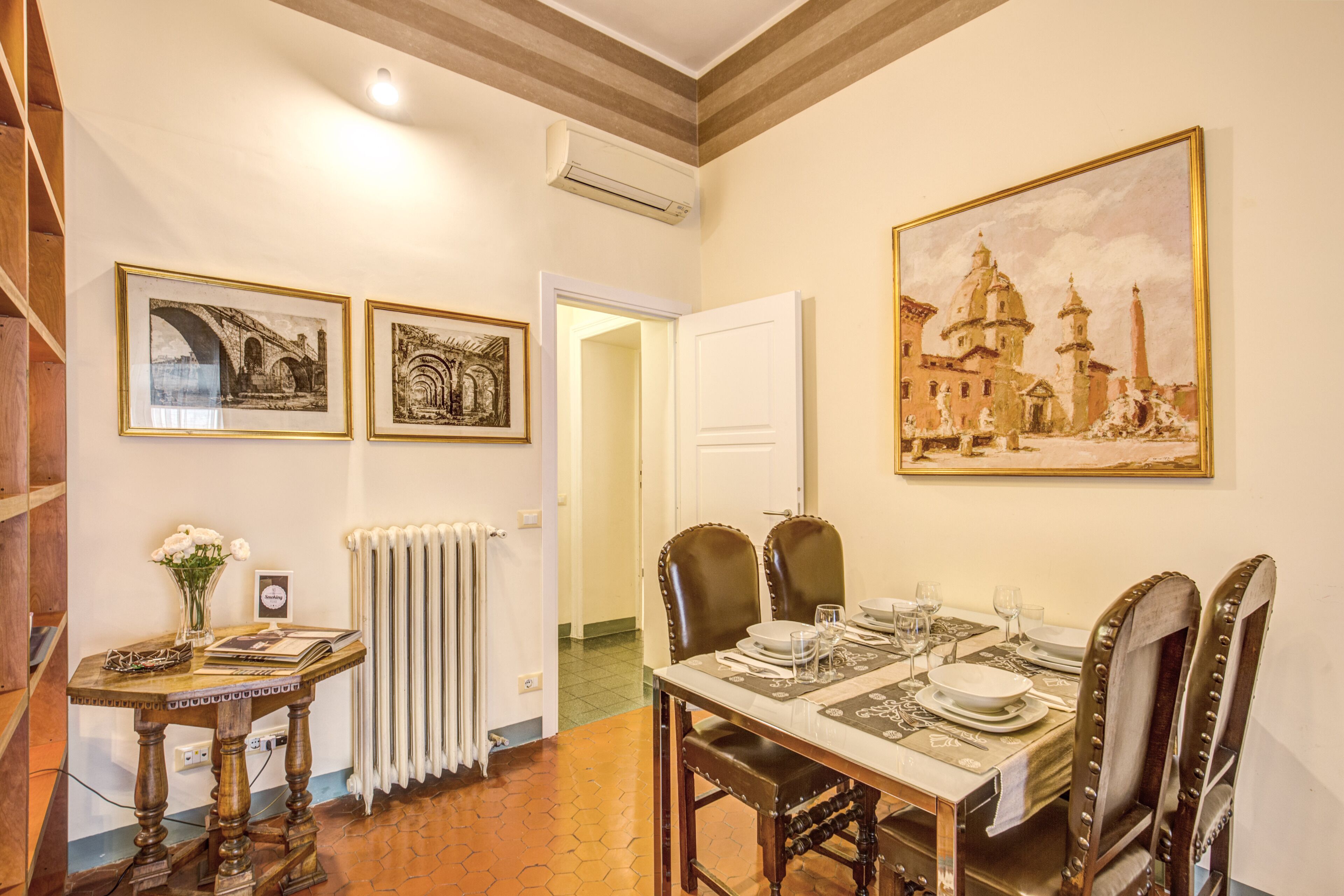 A dining area with a table set for four, two framed pictures on the wall, and a radiator on the wall.