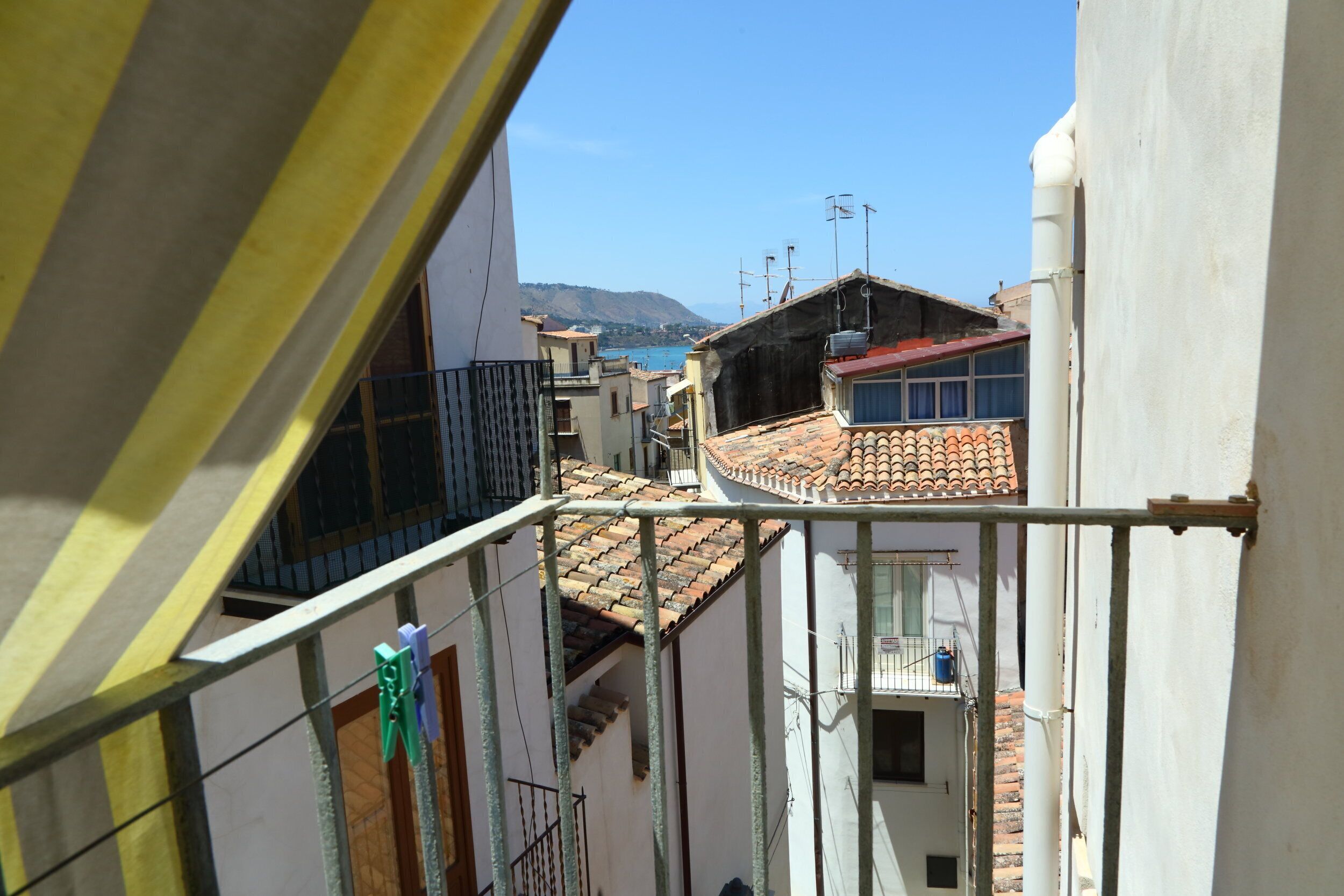 Une vue depuis un balcon donnant sur un quartier résidentiel, avec des toits recouverts de tuiles en terre cuite et un ciel bleu dégagé.