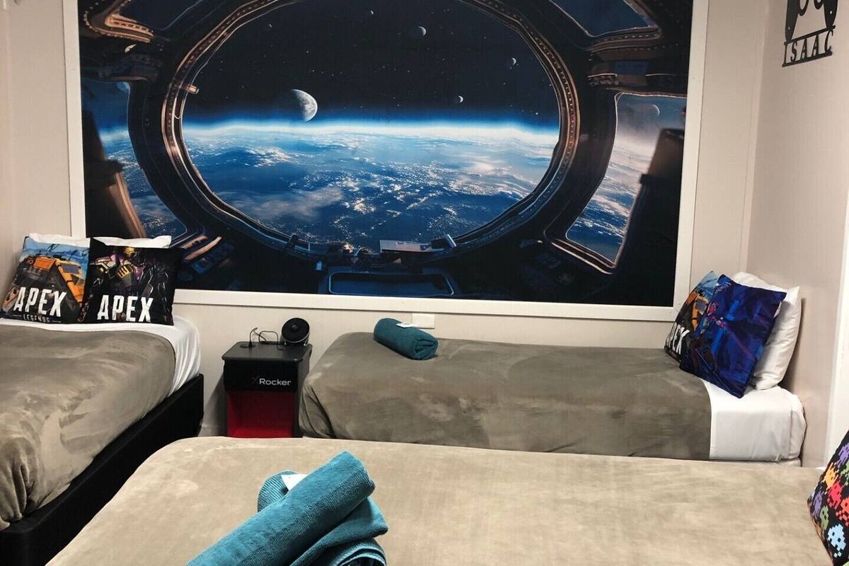 A bedroom with a space-themed wall art, a bed with a folded towel, a red heater, and a pillow with 'Apex Legends' text.