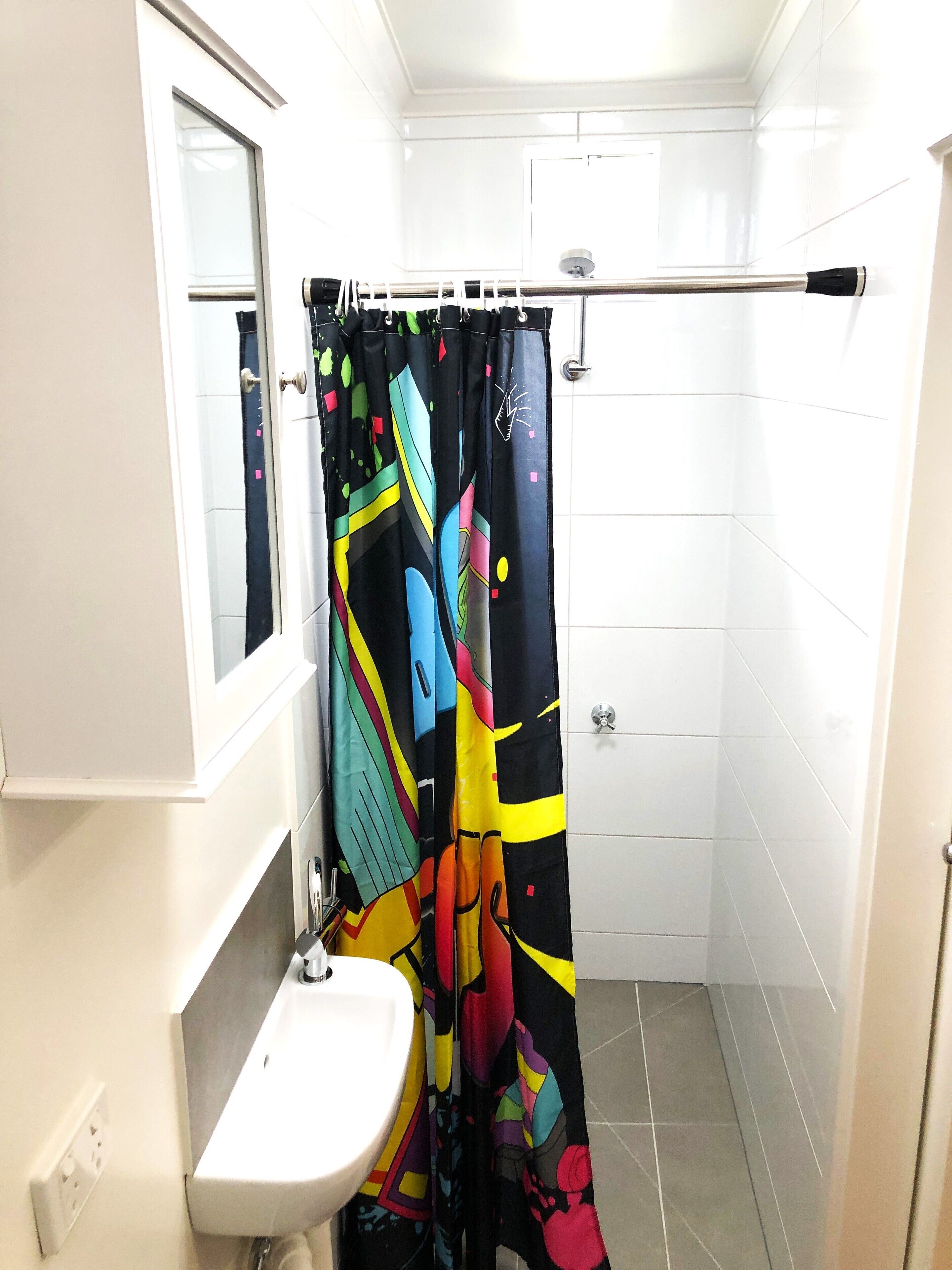 Un baño con un lavamanos blanco, un espejo y una cortina de ducha con un diseño abstracto y colorido.