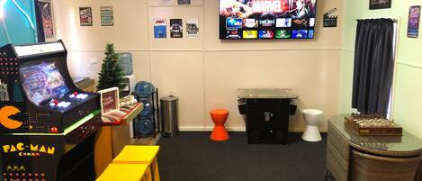A room with a Pac-Man arcade machine, a TV displaying Marvel movies, and a Christmas tree.