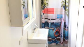 Un baño con un lavamanos blanco, un espejo encima, una cortina de ducha con diseño tropical y una alfombra azul y naranja en el suelo.