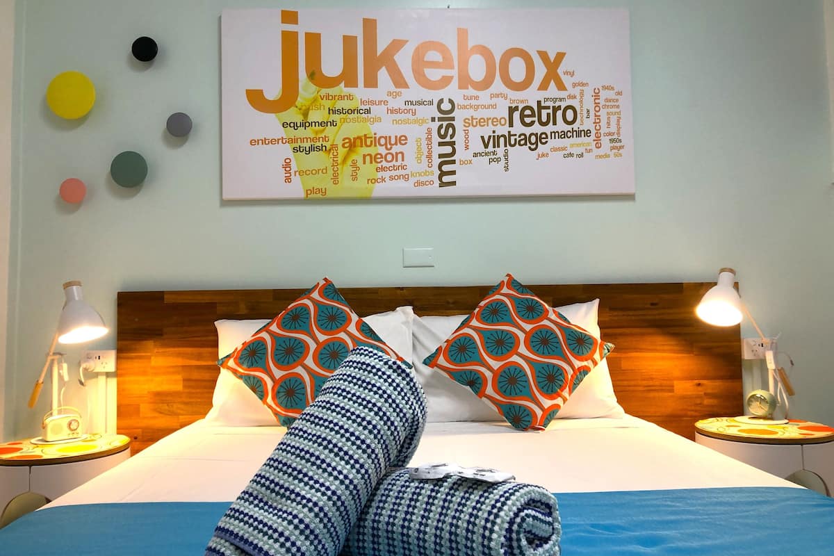 A hotel room with a bed, two bedside lamps, a rolled towel, and a word cloud on the wall.