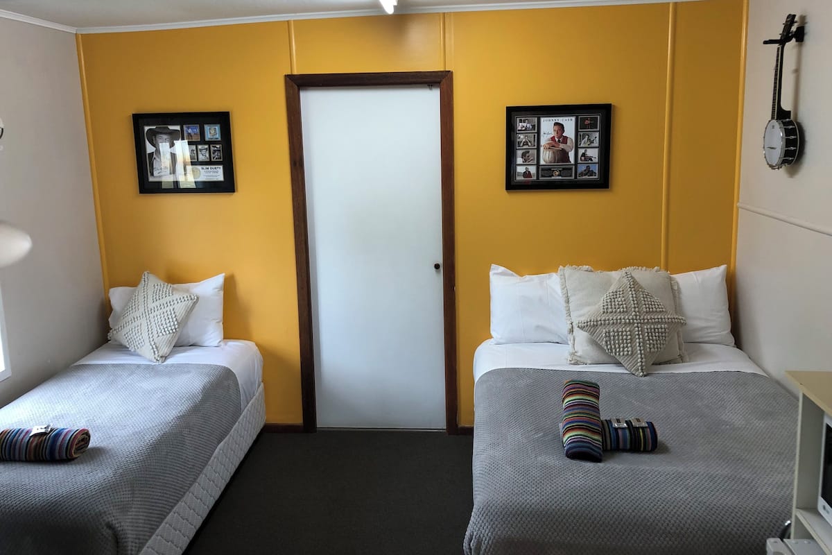 A hotel room with two single beds, a door, and a guitar on the wall.