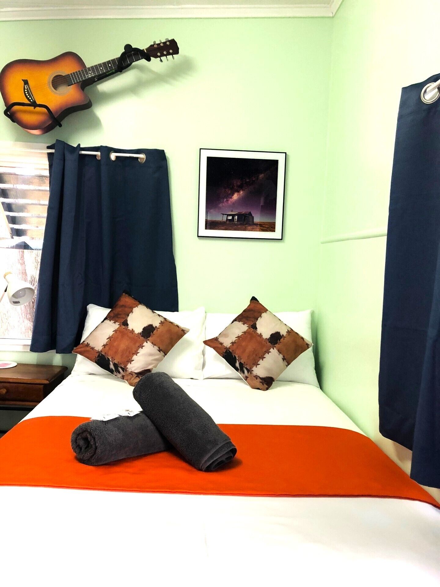 A room with a bed, a guitar, a framed picture, and a window with curtains.