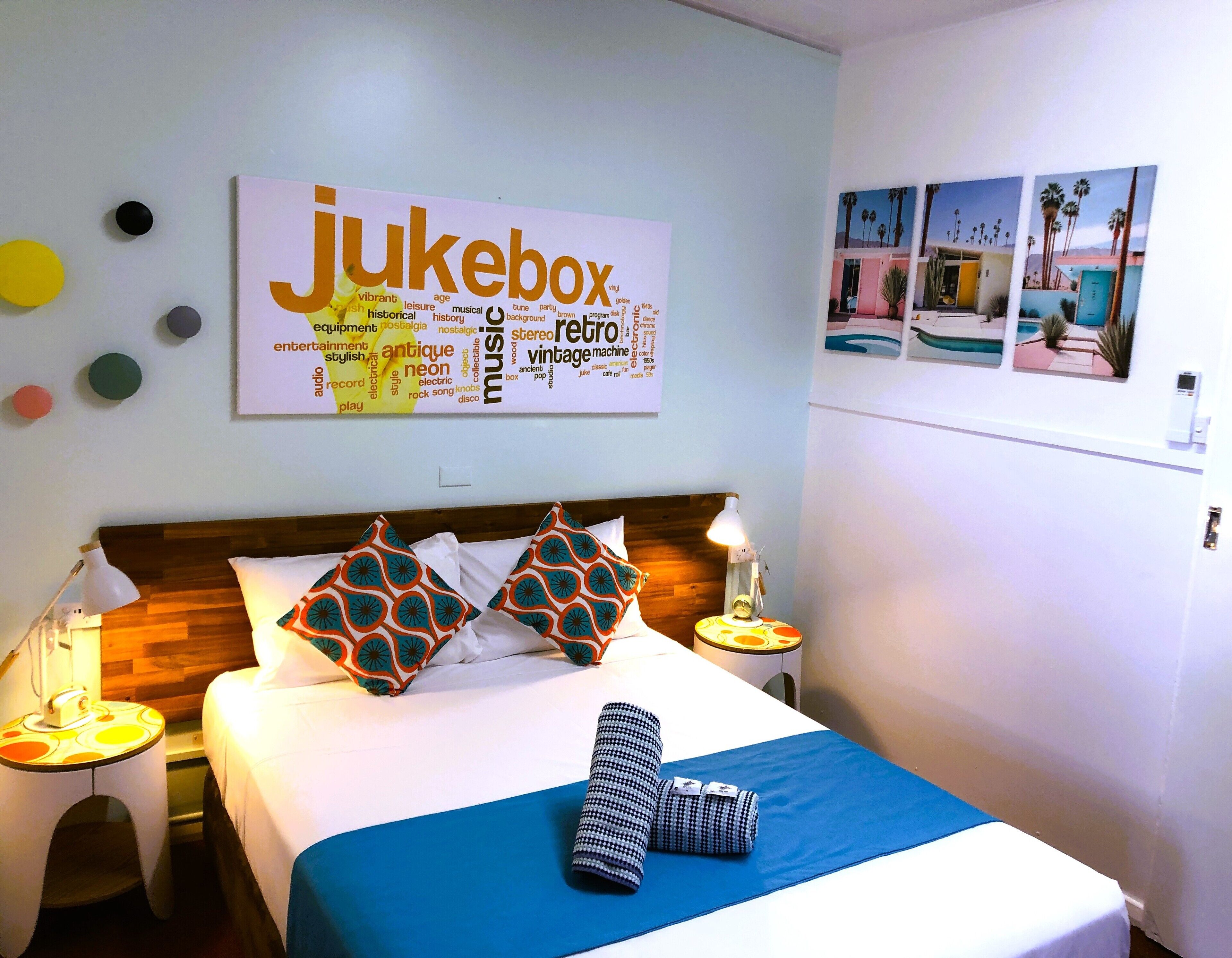 Ett hotellrum med en säng, kuddar, ett sängbord, en lampa och en vägg prydd med en affisch i form av ett ordmoln.
