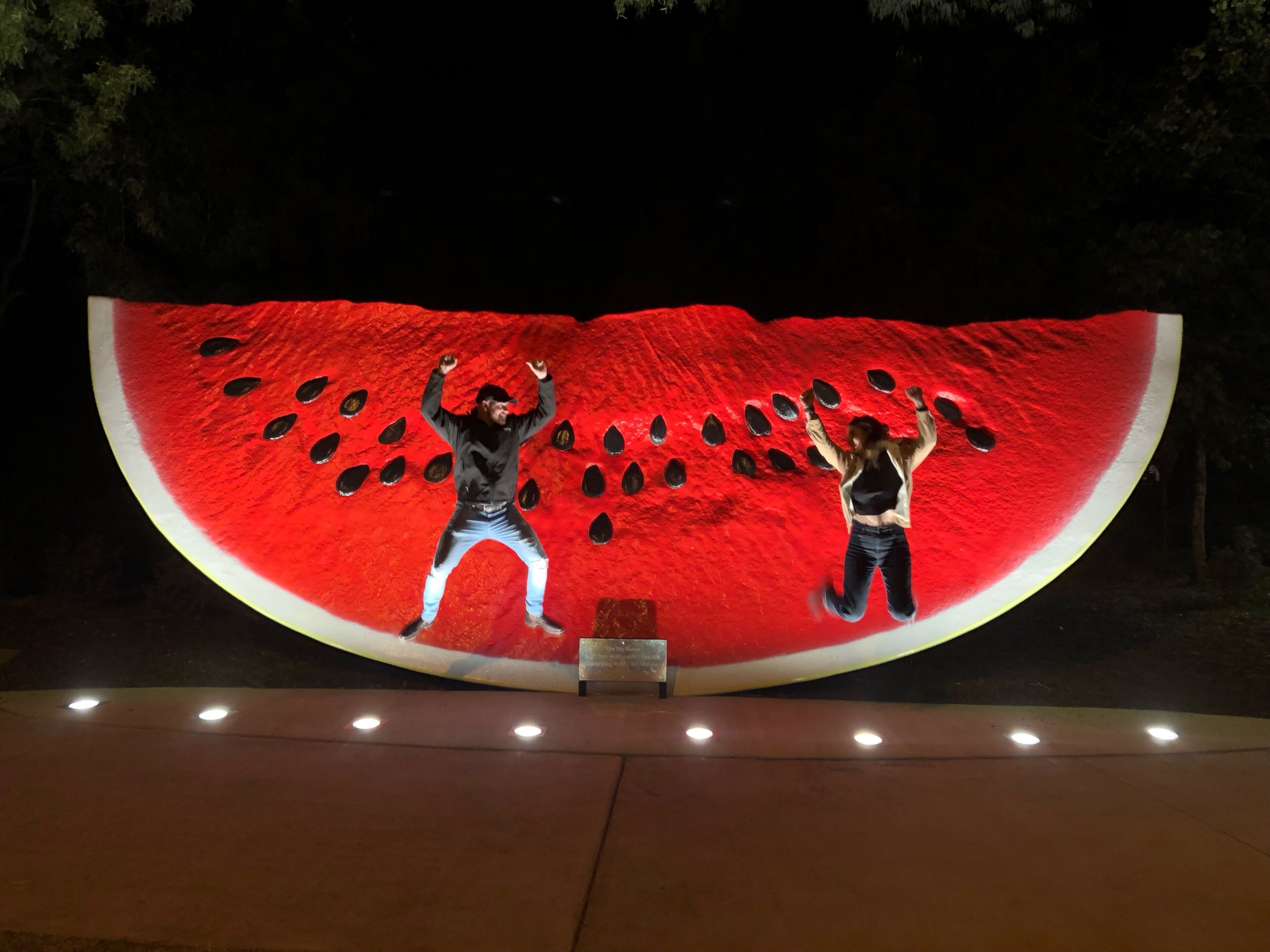 A large illuminated watermelon sculpture with two people posing in front.