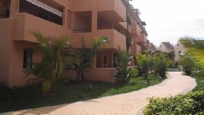 Un immeuble à plusieurs étages doté de balcons, entouré de verdure et bordé d’un sentier.