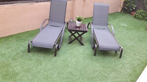 Deux fauteuils confortables, une petite table et un pot de fleurs placés entre eux, le tout installé sur une pelouse artificielle.