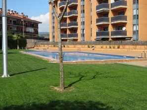 Une piscine entourée d’une pelouse bien entretenue, avec un immeuble à plusieurs étages en arrière-plan.