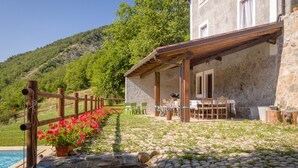 Un edificio in pietra con terrazza in legno, posti a sedere all'aperto e una piscina.