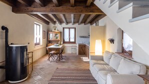 Un'ampia zona giorno con camino, tavolo da pranzo e divano. È presente anche un angolo cottura con lavello e pensili.
