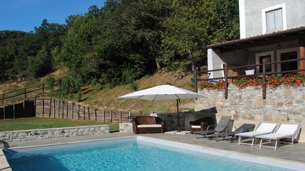 Una piscina con lettini e un ombrellone, circondata da muri in pietra e una recinzione in legno.