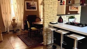 Une cuisine avec un mur en pierre, un coin bar avec des tabourets, une table à manger avec des chaises et un luminaire suspendu.
