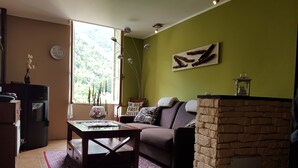 Un salon avec une table basse en verre, un canapé, une cheminée en pierre et une vue sur la verdure par une fenêtre.