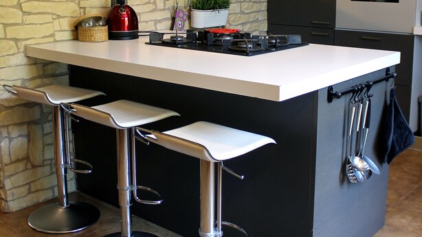 Une cuisine moderne dotée d’un îlot central, de tabourets de bar, d’appareils électroménagers en acier inoxydable et d’un mur d’accent en pierre.