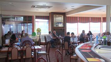 Un restaurant amb diverses taules i caires, grans finestres i una zona de mostrador.