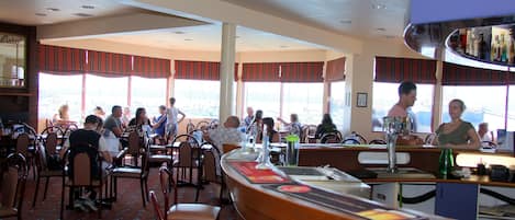 A restaurant with high tables and chairs, large windows, and a bar area.